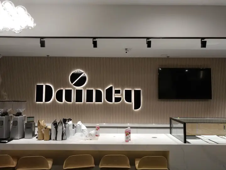 Illuminated Dainty Cafe lettering on a vertical slat wall.