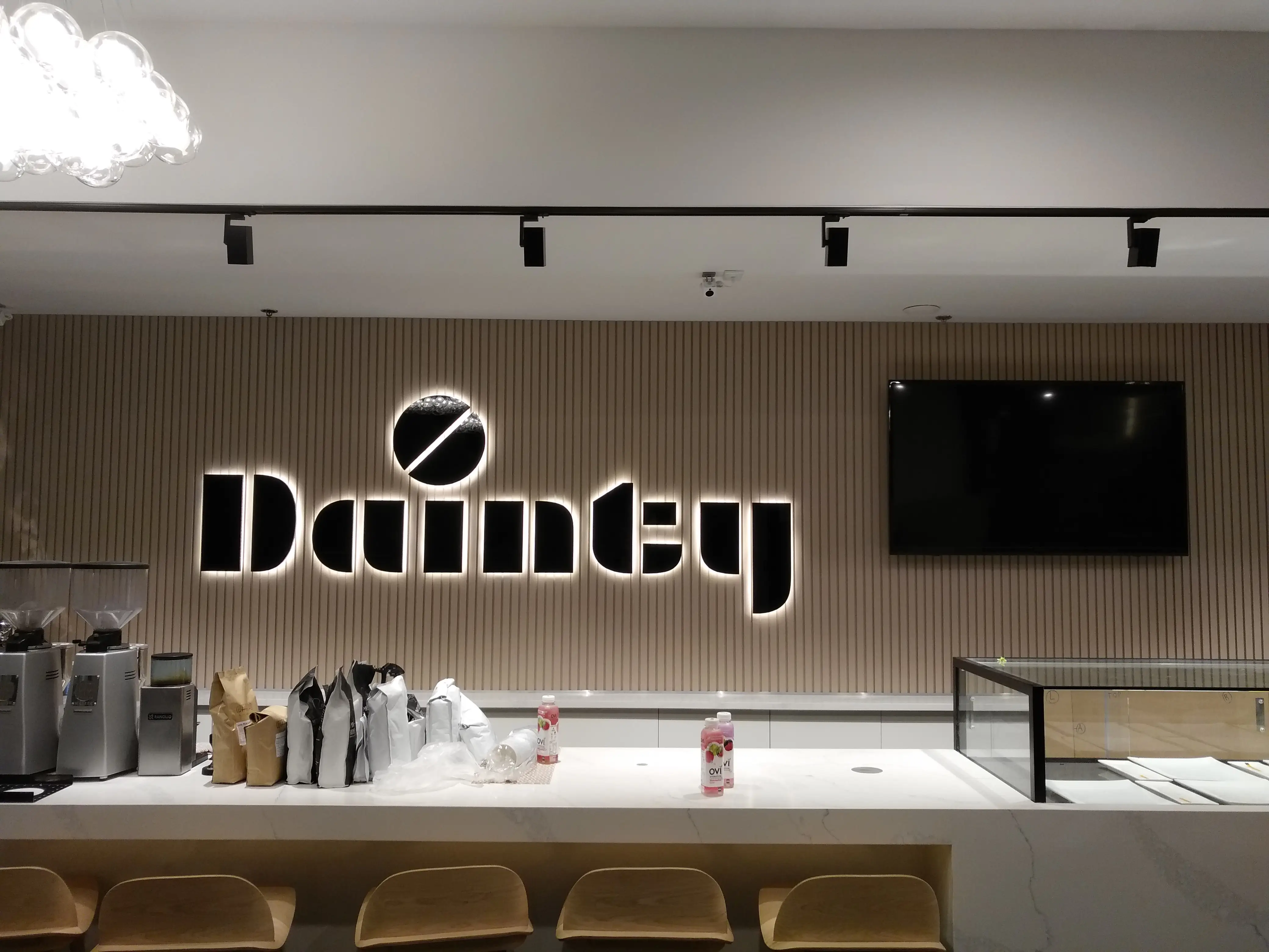 Illuminated Dainty Cafe lettering on a vertical slat wall.