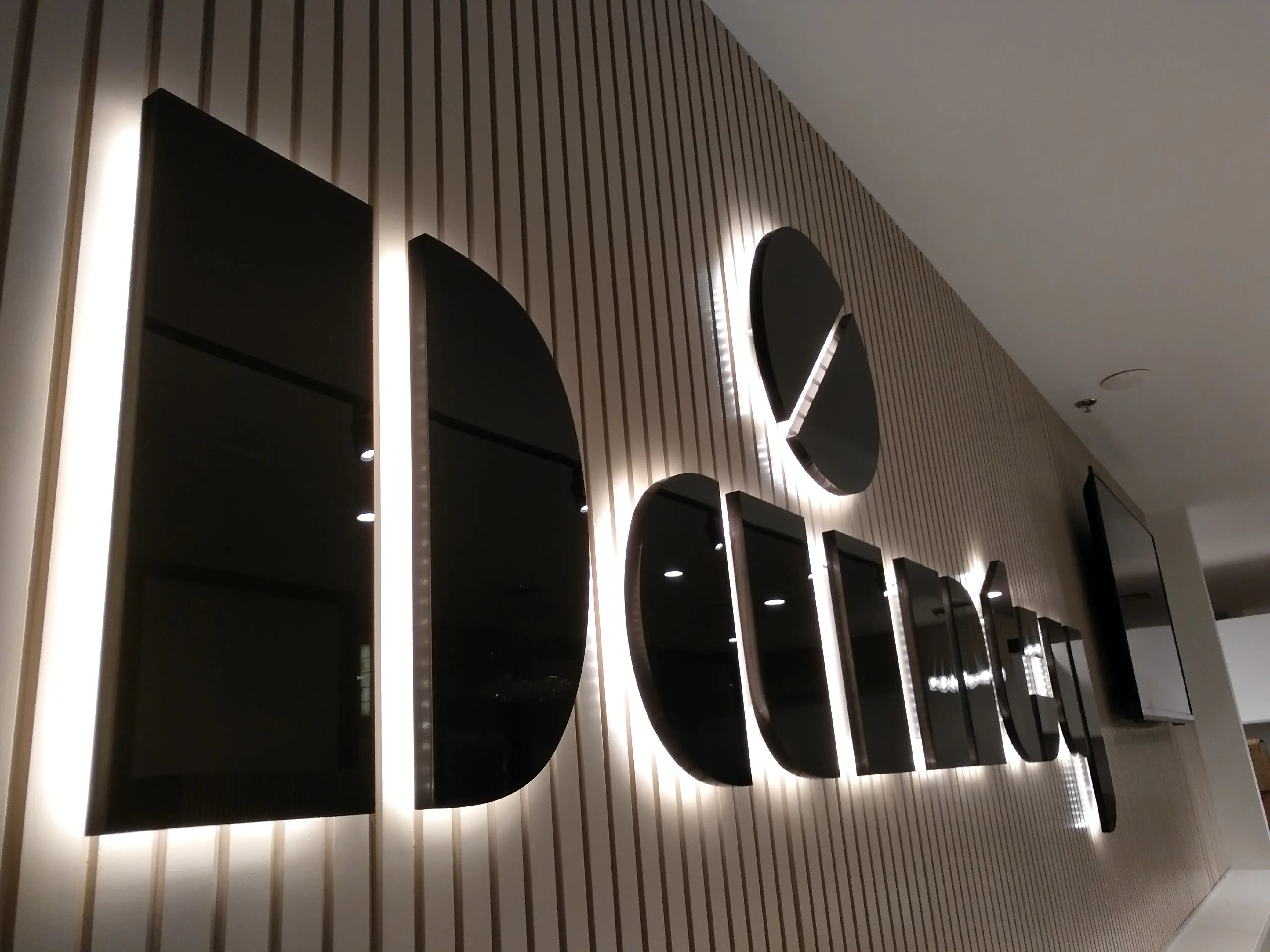 Illuminated Dainty Cafe lettering on a vertical slat wall.