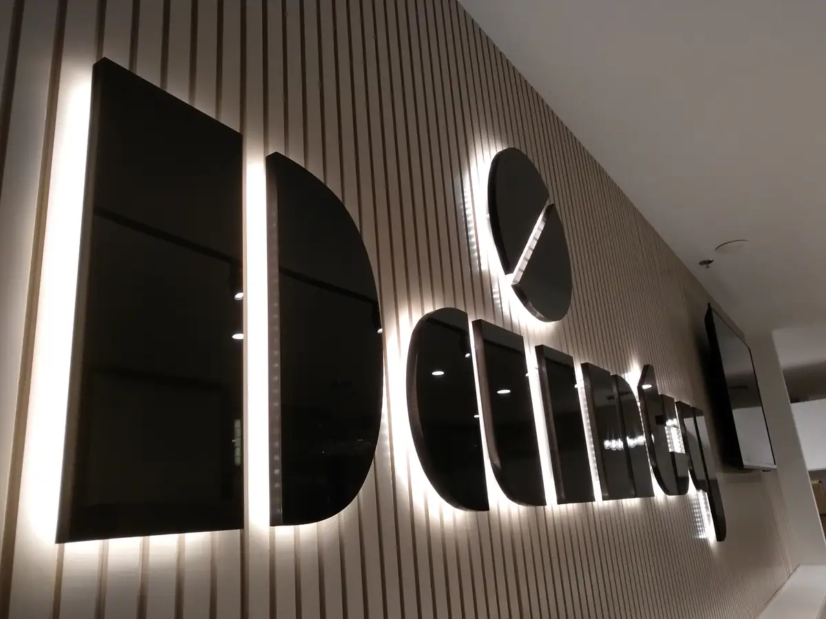 Illuminated Dainty Cafe lettering on a vertical slat wall.