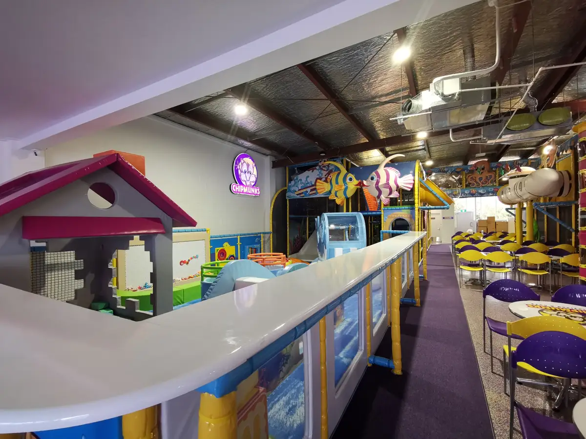 Low counter alongside the indoor play area, with café tables and yellow and purple seating.