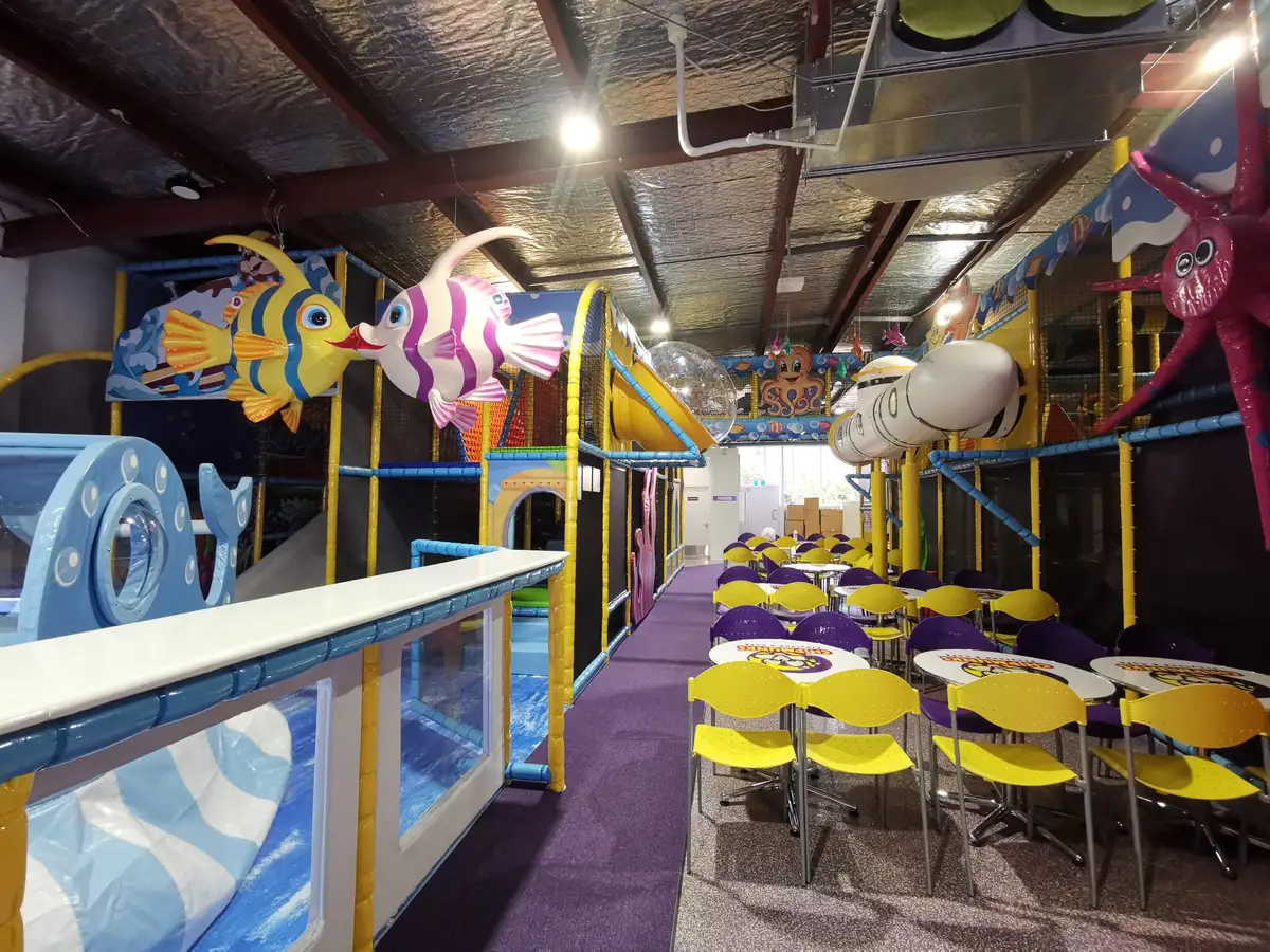 Colourful indoor play structures beside café tables and the central walkway.